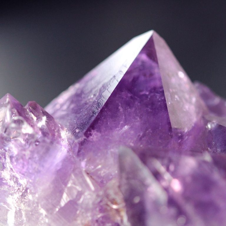Amethyst-Druse mit Kristallspitzen – Edelstein Lexikon Amethyst Amethyst-Druse mit violetten Kristallspitzen vor grauem Hintergrund – Symbolbild für die Kategorie Edelstein Lexikon Amethyst